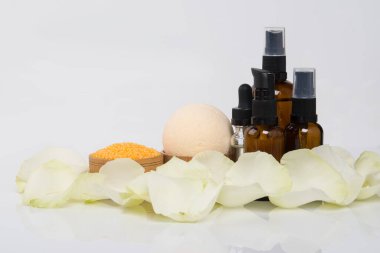 Beyaz bir arka planda, bir yazı için yeri olan dört şişe masaj yağı, gül yaprakları ve banyo tuzu ile çevrili.