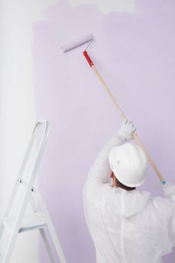 a worker in a helmet paints the wall purple