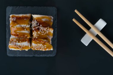 Siyah bir masa, üst manzara, yılan balığı, teriyaki sosu, susam tohumu ve ahşap çubuklar, yakın çekim.