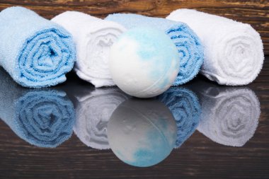 Yansıması olan karanlık bir ahşap arka planda, rulo içine sarılmış spa havluları ve tuz topu.