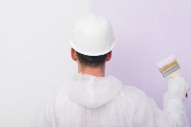 Duvarın önünde elinde fırçayla duvarı boyayan bir adam var.