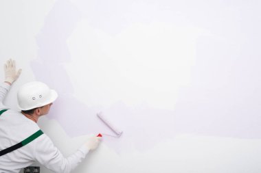 Duvarın köşesindeki bir işçi beyaz bölgelerin üzerini silindirle boyuyor.