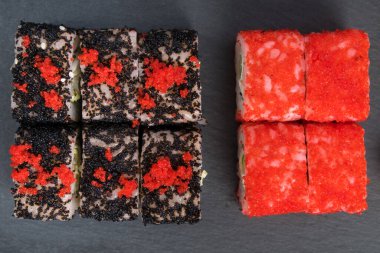 Karanlık bir masada, uçan balık havyarlı japon dürümleri, kırmızı ve siyah, üst görünüm