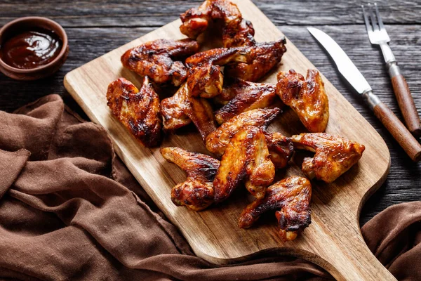 crispy fried chicken wings served on a wooden board with barbeque sauce on dark wooden table