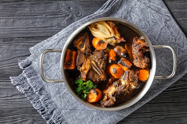 牛の骨の上に牛肉の肉のスープ遅いチャード野菜と調理 ニンジン タマネギ ニンニク スパイスは 木製のテーブル 上のビュー フラットレイアウト フリースペースの鍋で提供 — ストック写真