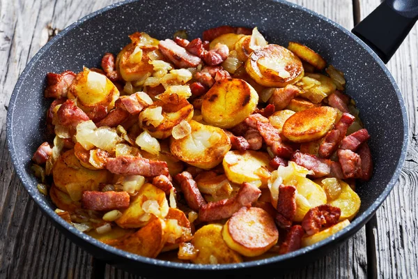 Bratkartoffelnのクローズアップ 木の素朴なテーブルの上に鍋にベーコンと玉ねぎとドイツの揚げジャガイモ — ストック写真