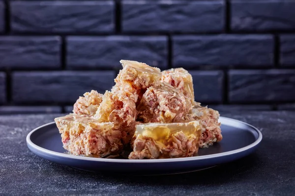 Traditional Russian meat aspic, jellied slow cooked meat on a plate on a concrete table with a black brick wall at the background