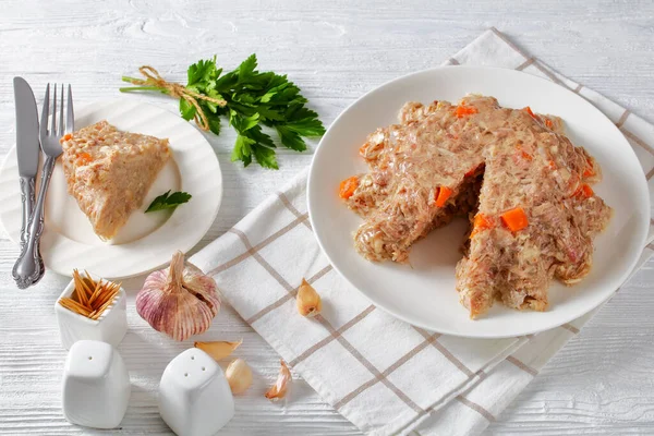 pork and chicken meat aspic, jellied slow cooked meat on a white plate on a wooden table