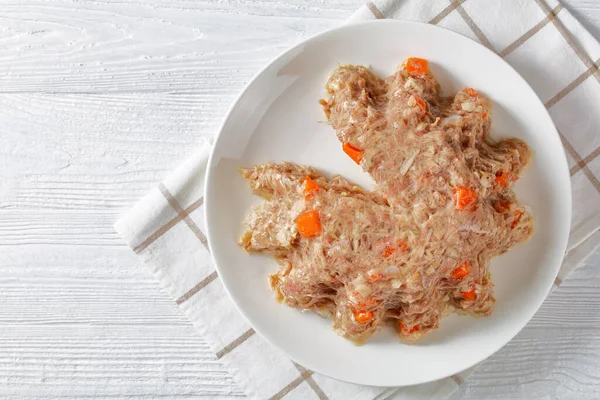 pork and chicken meat aspic, jellied slow cooked meat on a white plate on a wooden table, flat lay, free space