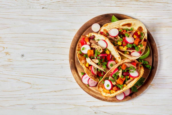 pitacos, mexican tacos with pita bread, spicy pulled chicken meat, red kidney beans, corn, radish, red pepper, roast sweet potatoes and lime on wooden board, flat lay, free space