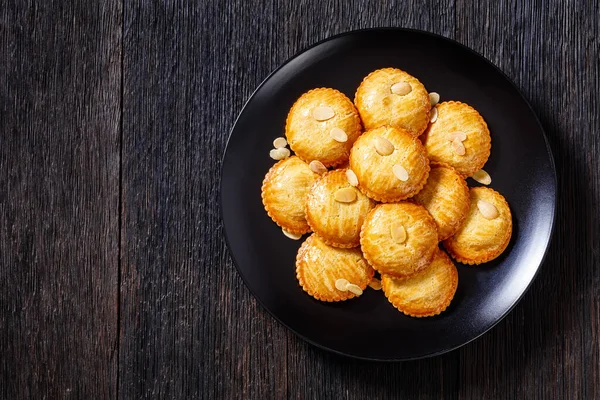 almond cookies filled with marzipan and almonds nuts paste, gevulde koek, on black plate on dark wood table, horizontal view from above, flat lay, free space