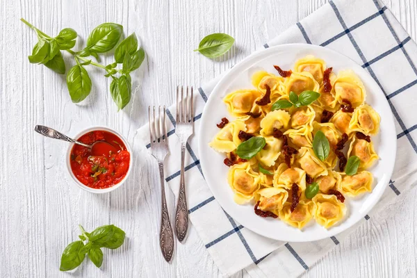 意大利多特利尼 用晒干的西红柿和意大利乳酪填充在白盘上 用新鲜罗勒和番茄酱放在白色质感桌子上 从上往下水平看 — 图库照片