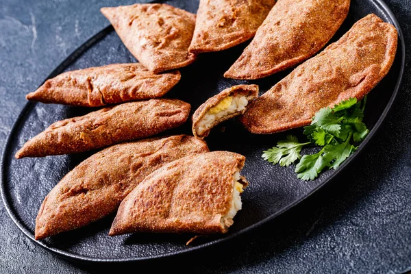 fried empanadas, hand pies with hard boiled egg fillings on black platter, horizontal view from above, close-up