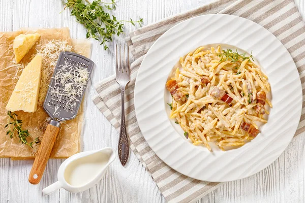 delicious capunti pasta in cream pecorino cheese and pancetta sauce in white bowl with ingredients on white wooden table, italian cuisine, horizontal view above, flat lay