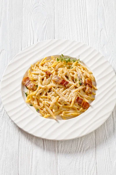 delicious capunti pasta in cream pecorino cheese and pancetta sauce on white plate on white wooden table, italian cuisine,vertical view above