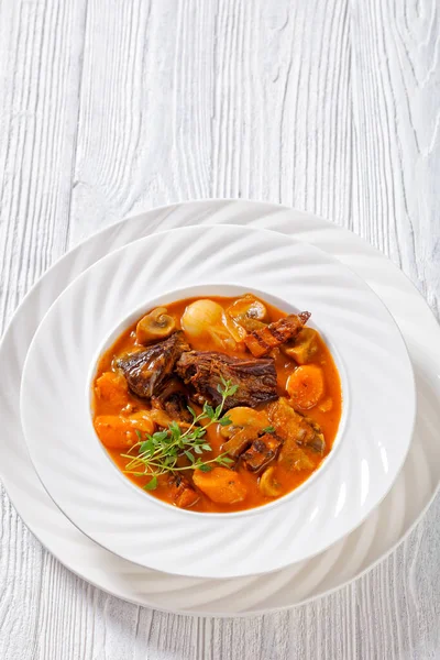 Beef Bourguignon, Beef Burgundy, stew with beef, bacon, carrots, onions and mushrooms slow cooked in rich red wine sauce in white bowl, french cuisine, vertical view, free space