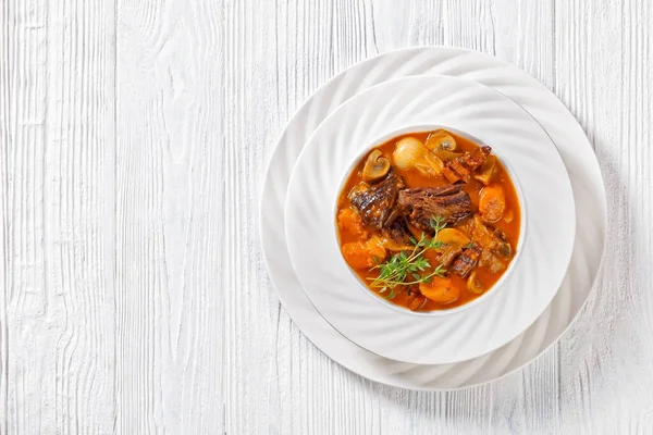 Beef Bourguignon, Beef Burgundy, stew with beef, bacon, carrots, onions and mushrooms slow cooked in rich red wine sauce in white bowl, french cuisine, horizontal view, flat lay, free space