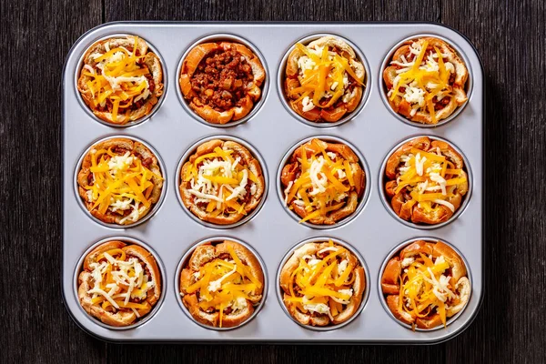 sloppy joe cups, hamburger bun cups with ground beef and onions tossed in sloppy joe sauce and topped with cheese in muffin tin on dark wooden table, horizontal view from above, flat lay, close-up