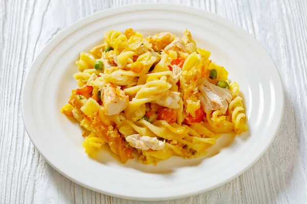 Chicken Pot Pie Fusilli pasta casserole with celery, corn, green peas, carrots, topped with panko breadcrumbs on white plate on white wood table, horizontal view from above