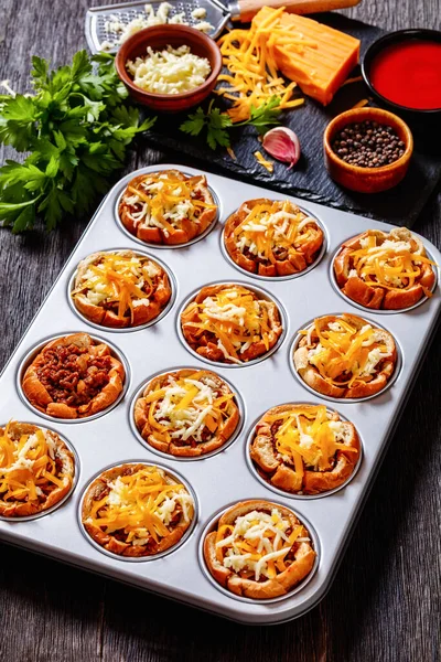 sloppy joe cups, hamburger bun cups with ground beef and onions tossed in sloppy joe sauce and topped with cheese in muffin tin on dark wooden table, vertical view from above, close-up