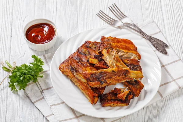 Fall Off the Bone Oven Baked Ribs on white plate on white wooden table with ketchup