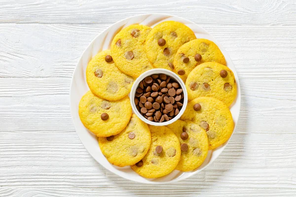chocolate chip lemon yellow cookies on white plate on white wood table, american cuisine, horizontal view from above, flat lay, close-up