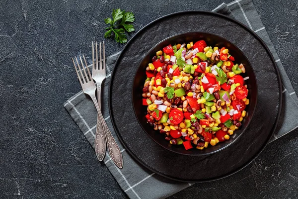 Black Bean Salad with Black-Eyed Peas, pepper, red onions, corn, cherry tomatoes and cilantro in black bowl, flat lay, free space