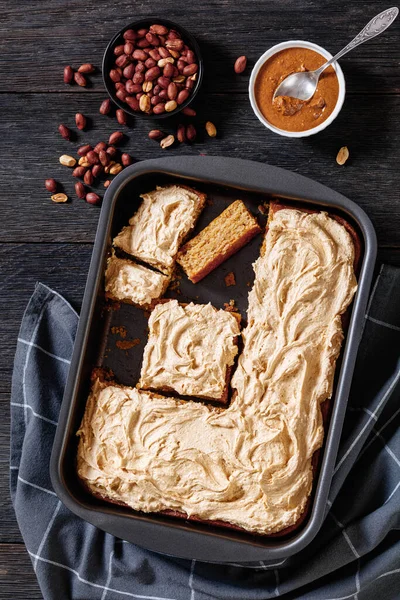 Peanut Butter Sheet Cake topped with super creamy and sweet peanut butter icing in a baking dish and a portion on plate, vertical view from above, american dessert