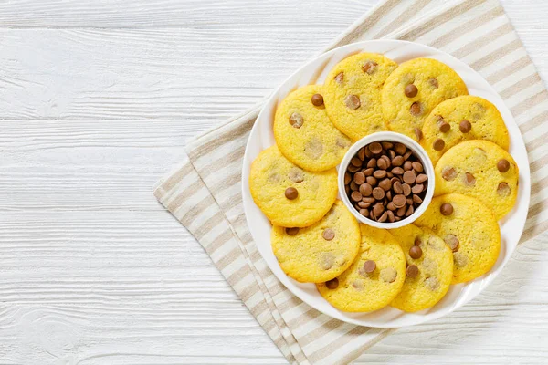 chocolate chip lemon yellow cookies on white plate on white wood table, american cuisine, horizontal view from above, flat lay, free space