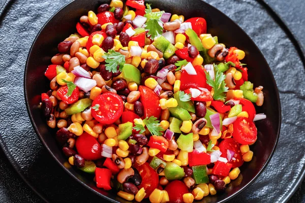 close-up of Black Bean Salad with Black-Eyed Peas, pepper, red onions, corn, cherry tomatoes and cilantro in black bowl