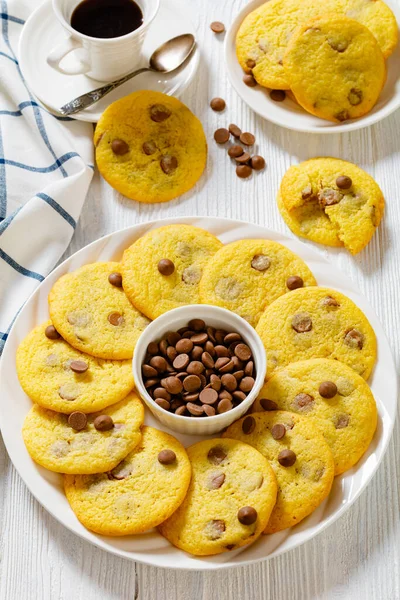 chocolate chip lemon yellow cookies on white plate on white wood table with cup of black coffee on background, american cuisine, vertical view from above