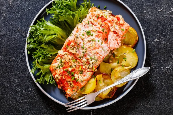 roast salmon with sliced baked potato. fresh lettuce and tarragon horseradish sour cream sauce on plate on concrete table, horizontal view from above, flat lay, close-up