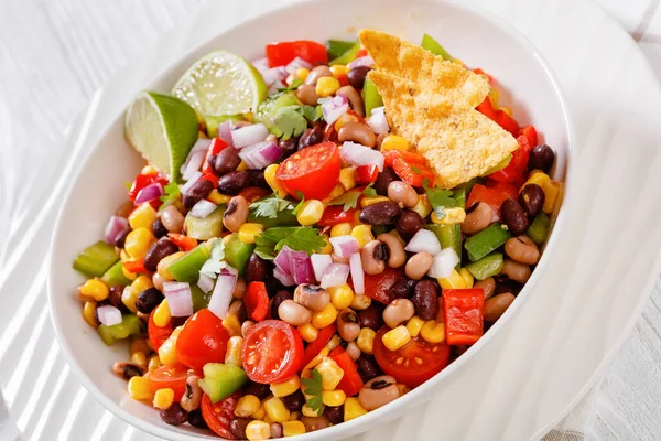 Black Bean Salad with Black-Eyed Peas, pepper, red onions, corn, cherry tomatoes and cilantro in white bowl with tortilla chips, nachos, close-up