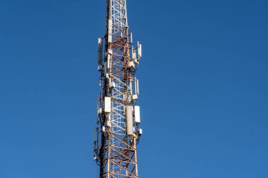 Mavi gökyüzüne karşı birden fazla anteni olan cep telefonu kulesi