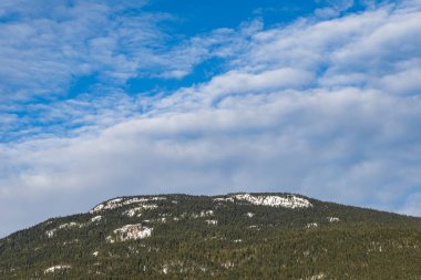 Büyük dağ, mavi gökyüzü ve beyaz bulutlarla kaplı yeşil ormanla kaplı İngiliz Kolombiyası Kanada.