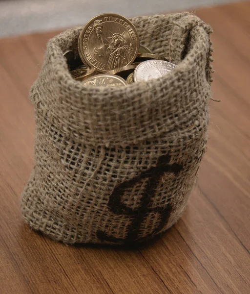 Çuval çantasındaki dolar paraları ve ahşap masada dolar işareti.