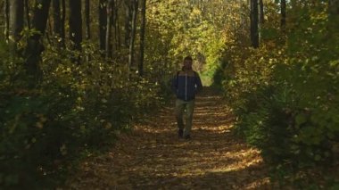 Sırt çantalı olgun bir turist nehir kenarındaki sonbahar ormanında yürüyor.