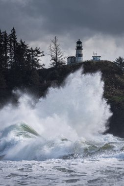 Washington sahilindeki gelgit fırtınası sırasında, Cape Hayal kırıklığı Eyalet Parkı 'nda deniz fenerinin altında büyük bir dalga var.