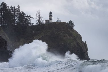 Washington sahilindeki gelgit fırtınası sırasında, Cape Hayal kırıklığı Eyalet Parkı 'nda deniz fenerinin altında büyük bir dalga var.