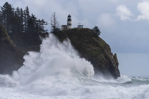 Large stormy wave crashing under cliff and lighthouse on the Washington Coast at Cape Disappointment, Pacific Northwest United States