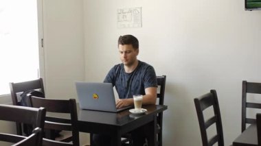 Bir adam kafede dizüstü bilgisayarda çalışıyor.