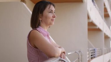 Balkonda yaz tatilinin tadını çıkaran genç bir kadın. Gülümseyen kadın ellerini otel terasındaki korkuluklara koyar..