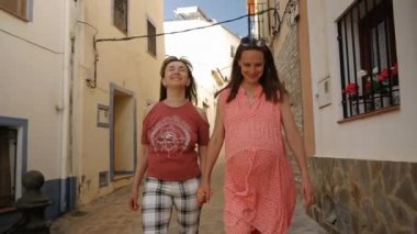 Happy gay female couple strolling through the town. Pregnant woman smiles holding her partners hand. LGBT surrogate concept