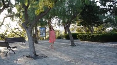 Young pregnant woman wearing summer dress walking in the park. Wide shot.