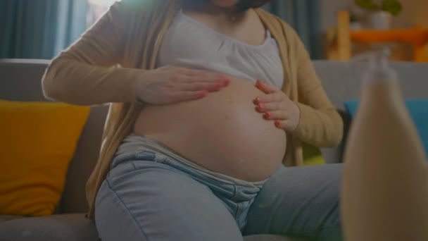 Onherkenbare zwangere jonge vrouw gebruikt zalf of bodylotion — Stockvideo