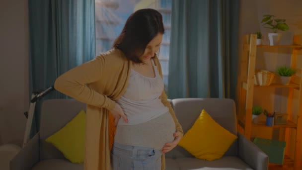 Młoda kobieta w ciąży odczuwa dyskomfort w dolnej części pleców na tle środowiska domowego — Wideo stockowe