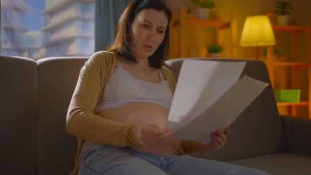 Έγκυος νεαρή γυναίκα με κομμάτια χαρτιού στα χέρια της λαμβάνει άσχημα νέα ή δοκιμές κλαίει καλύπτει το πρόσωπό της με τα χέρια της — Αρχείο Βίντεο
