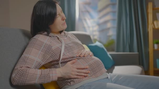 Seorang wanita hamil sedang duduk di sofa dan mengalami ketidaknyamanan — Stok Video