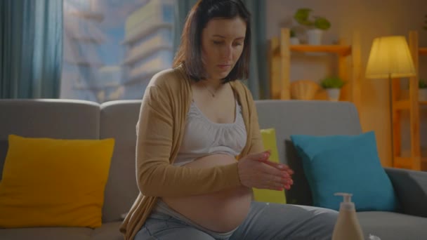 Mujer joven embarazada utiliza ungüento o loción corporal — Vídeos de Stock