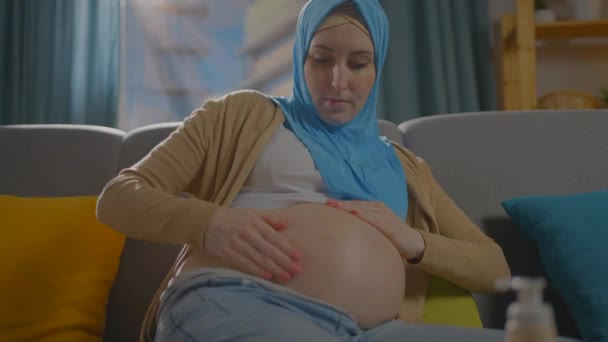 Schwangere muslimische junge Frau verwendet Salbe oder Körperlotion — Stockvideo